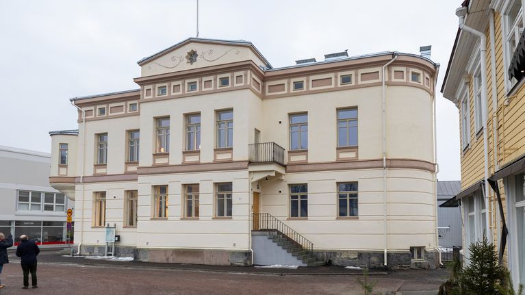 Ett stort ljust stenhus i gammal stil vid ett torg.