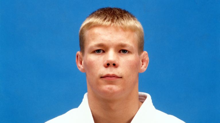 Judoka Jorma Korhonen katsoo kameraan judoasussa sinistä taustaa vasten.