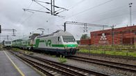Ett VR-tåg anländer till Karis järnvägsstation en mulen dag. I bakgrunden syns ett stort byggnadskomplex med texten "AXXELL" på fasaden.