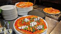 Pizza tulossa uunista, etualalla näkyy Pizzeria Napolin Burrata-pizza.