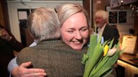 Pia Sillanpää hymyilee onnellisena tulppaanit käsissä kun häntä halaa harmaahiuksinen henkilö.