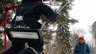 Lapsi keinussa etualalla ja mies antamassa vauhtia.