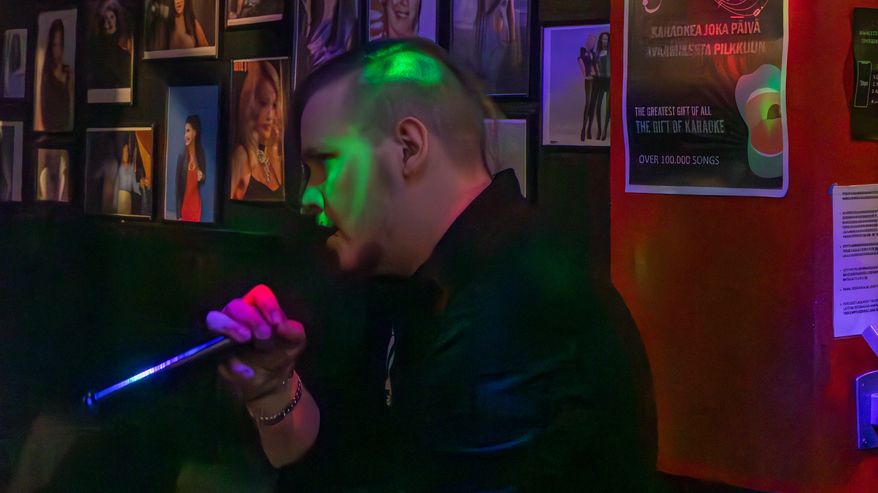 Mies laulaa karaokea ja hänen yläpuolellaan näkyy televisio, jossa on karaoke-laulun sanat.