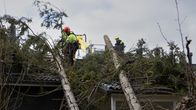 Kaksi suurta kuusta on kaatunut rivitalon päälle. Pelastuslaitoksen henkilökunta on katolla poistamassa puita.