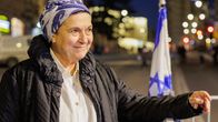 Huivipäinen nainen nojaa kädellään kadulla olevaan metalliaitaan.