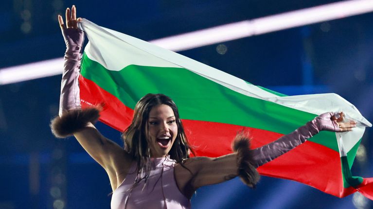 En kvinna i en rosa topp och handskar ler medan hon håller i Bulgariens flagga.