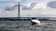 A speedboat on the water with a long bridge in the background.