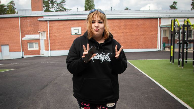 Yläasteikäinen Selma Rannikko seisomassa koulun pihalla. Rannikko mutristaa huuliaan ja näyttää sormillaan rauhan merkkiä. Jalassaan hänellä on Hello Kitty -yöhousut.