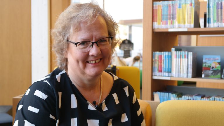 Lena Marander-Eklund  sitter framför en bokhylla.