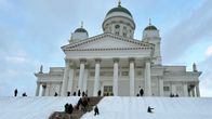 Helsingin tuomiokirkko talvisena päivänä. Kirkon edessä rappusilla on lunta ja ihmiset laskevat pulkalla siinä.