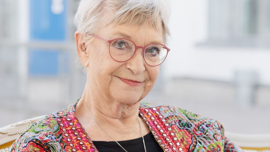 Tuula Karjalainen istuu sohvalla ja pitelee käsissään uusinta kirjaansa, katsoo sivusilmin kohti kameraa.