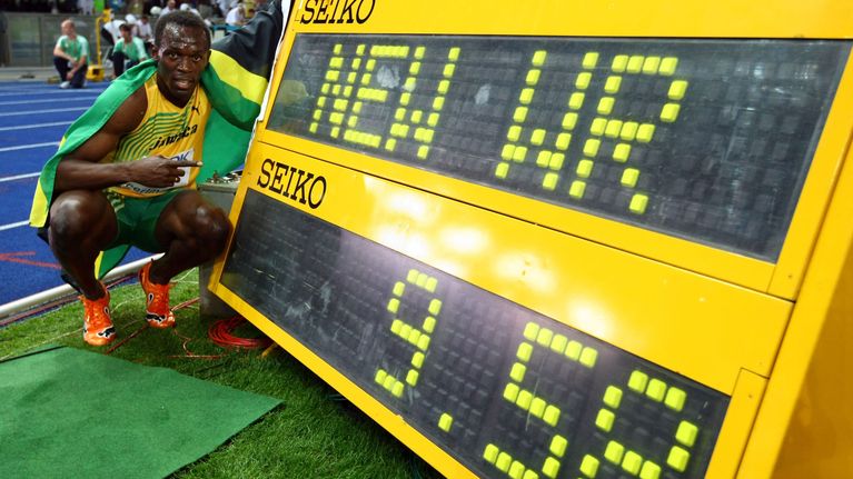 Usain Bolt sitter på huk  bredvid en stor resultatskylt med siffrorna 9.58.