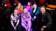 6 personer sitter på golvet i en tv-studio, och ser in i kameran och ser glada ut.