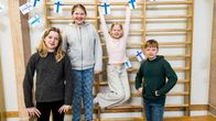 Fyra skolever står framför en vägg med ribbstolar. Finska flaggor hänger på väggen.