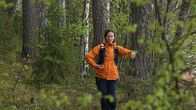 Tanssija Sanna Hento oranssissa takissa tanssimassa metsä taustanaan.