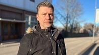 En man med grått bakåtkammat hår och grå skäggstubb ute vid en gata. Han ser allvarlig ut.
