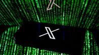 X-logo puhelimen näytöllä. Taustalla on matrix-tyylinen vihreä koodijono.
