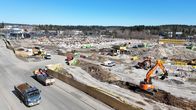 Kuvassa on rakennustyömaa, kuvattuna ilmasta. Työmaalla on kaivinkoneita, kuorma-autoja ja hiekkakasoja. 