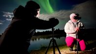 A man films a woman who films the aurora borealis. 