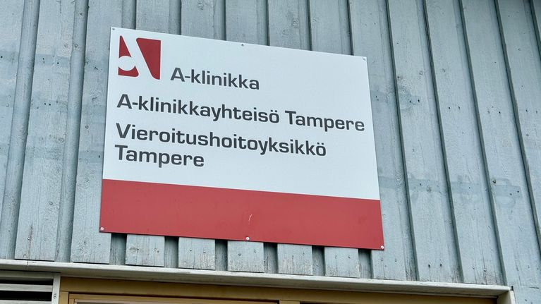 A red-and-white sign for an A-Clinic detox centre in Tampere, attached to a light-blue wooden wall.