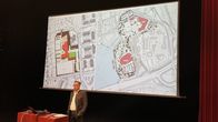 Mies seisoo suuren valkokankaan edessä. Valkokankaalla on kaksi karttakuvaa, joissa on Mikkelin mahdollisia kouluratkaisusuunnitelmia.