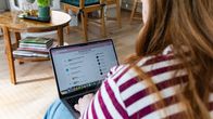 A woman sat with a laptop in her lap. On the laptop screen is a list of job listings.