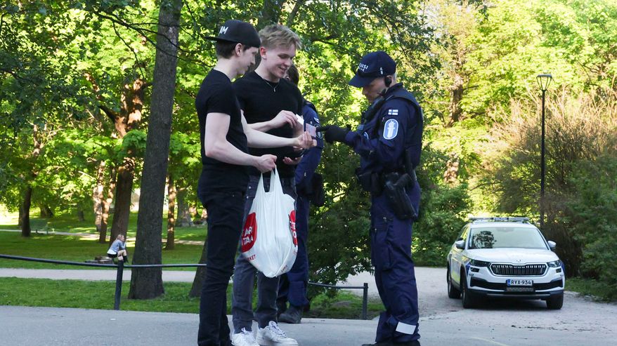 Poliisi tarkastaa kahden muovikassia kantavan nuoren henkilöllisyystodistukset puistossa.