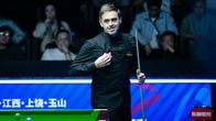 Snooker-pelaaja katsoo maila kädessä pöytää.