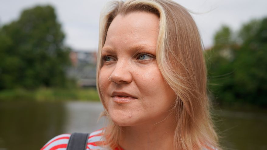 Lähikuvassa raitapaitainen ja vaaleahiuksinen nainen katsoo kaukaisuuteen.