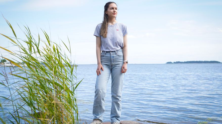 Nuori nainen seisoo rantakivellä ja katsoo kaukaisuuteen.