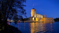 Olavinlinna hehkuu iltavalaistuksessa iltahämärässä Saimaan rannalla Savonlinnassa.