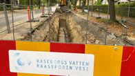 En gul grävmaskin vid en delvis uppgrävd gata. I förgrunden står det "Raseborgs vatten Raaseporin vesi" på en skylt. Hus och träd syns också.