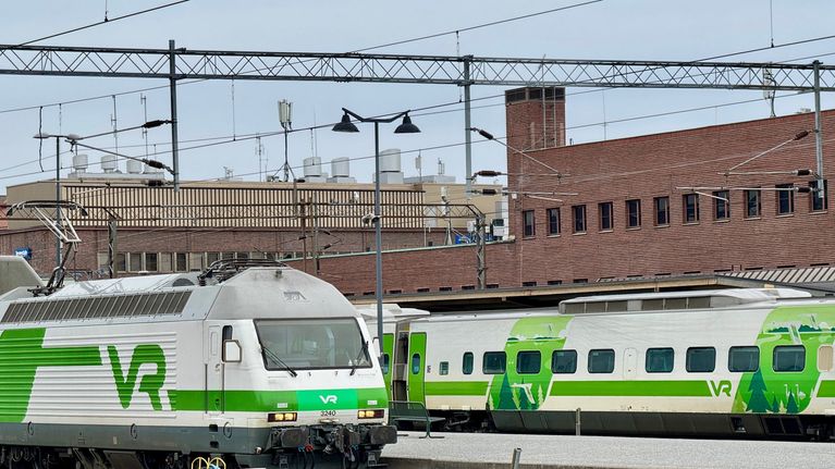 Två ståg mellan perrongerna på en station med rödtegelbyggnader.