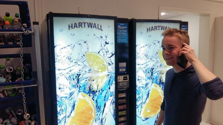 Gymnasieeleven Rasmus Östdahl står med telefon i hand och beställer läsk från en varuautomat i skolan.