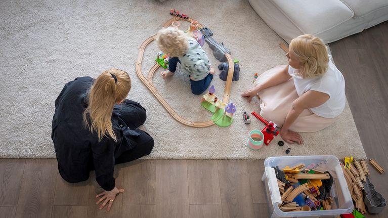 Lapsi leikkii lattialla junaradalla vanhempiensa kanssa.