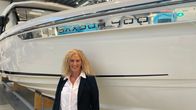 En blond kvinna med svart kavaj står framför en stor motorbåt i en industrihall.
