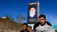 Kaksi henkilöä kävelee Ali Khamenein muistomainostaulun vieressä.
