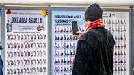 En person tittar på och fotograferar en anslagstavla med kandidater inför ett val i Finland.
