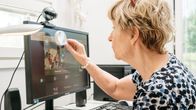 Nainen katsoo suurennuslasilla tietokoneen näyttöä.