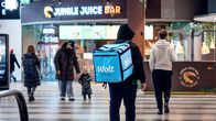Wolt-lähetti kävelee Kampin kauppakeskuksessa. Taustalla muita ihmisiä ja Jungle Juice Barin kyltti.