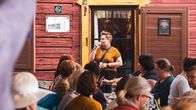 Nainen puhuu mikrofoniin yleisön edessä.