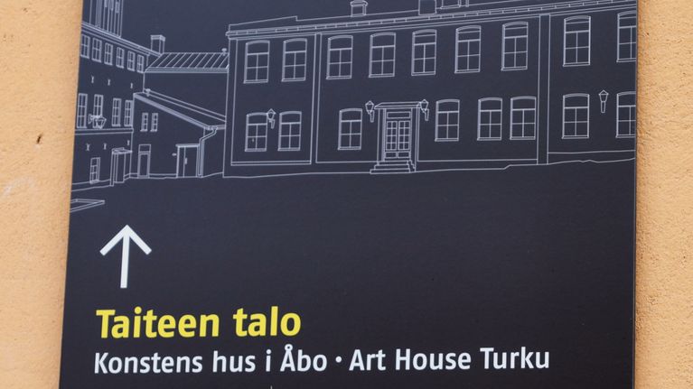 Svart skylt med illustration av byggnader och text som visar vägen till Taiteen talo, Brinkkala, Hjelttin talo och Juseliuksen talo.