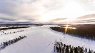 Ilmakuva Sodankylän Viiankiaavasta talvella. Lumista aukeaa, metsää, aurinko pilkistää pilvien raosta.