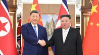 Kaksi pukupukuista miestä kättelee Pohjois-Korean ja Kiinan lippujen edessä juhlavassa sisätilassa. Taustalla on maisemamaalaus.