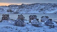 Taloja kahdessa rivissä meren rannalla. Maassa on lunta, taustalla näkyy merta ja vuoria.