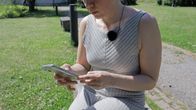 Kvinna som sitter på bänk och ringer samtal med mobiltelefon. 