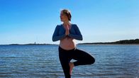 En kvinna med gravidmage som står i en yogaposé med vatten och öar i bakgrunden.