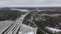 Talvinen maisema moottoritieltä, missä tiet ja ympäröivä luonto ovat lumen peittämät. Taustalla näkyy laajoja metsiä ja peltoja sekä pilvinen taivas.