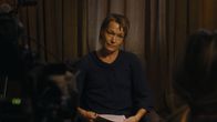 En person sitter framför kameran för en intervju eller inspelning, håller papper och har en mörkblå tröja.
