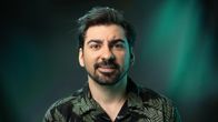 Gogi Mavromichalis katsoo kameraan, taustalla tummanvihreä tausta.